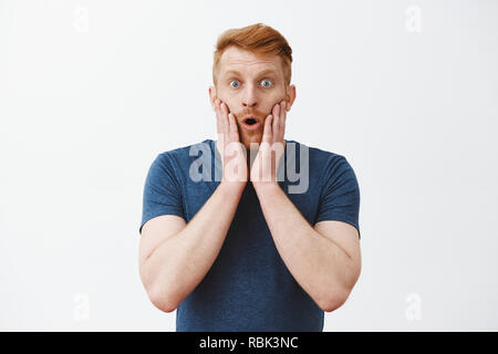 Attractive Caucasian redhead man with bristle expressing surprised and amazement, touching face and folding lips, standing in stupor and popped eyes at camera, being under impression Stock Photo