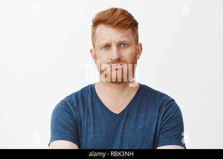 Studio shot of attractive adult caucasian redhead guy with bristle, pursing lips and frowning being troubled to answer, stuck in tough and annoying situation, breathing out, feeling questioned Stock Photo