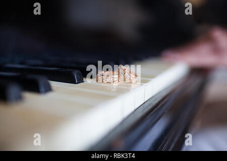 A pair of wedding rings are on the keys of the black piano. In the background in the blur a female hand is discernible, lying on the keys. Stock Photo