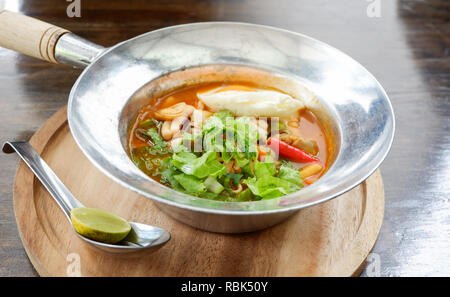 Sour soup with seafood shrimp squid / Hot and sour soup fish , egg and lettuce vegetable in hot pot on wooden tray dining table - Thai food curry soup Stock Photo