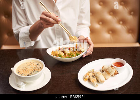 Lady in white blouse sitting in luxury restaurant and eating tasty meal. Three courses lunch from soup, noodles and tempura shrimps on special offer. Girl tasting oriental style dish. Stock Photo