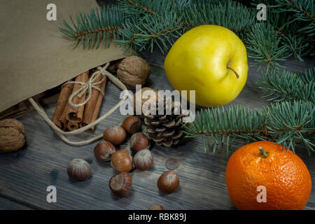 Various nuts, cinnamon yellow apple and clementine as concept of holiday groceries, spread on wooden table out of paper shopping bag, viewed in close- Stock Photo