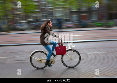 Female cyclist on an Amsterdam road using a mobile phone. Stock Photo
