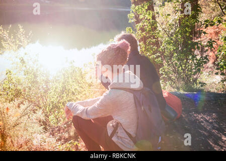 Side view of two male friends, relaxing and watching scenery on fresh air in wild wood near lake in day sun light. Travel autumnal adventure. Tourist  Stock Photo