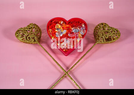 Red glowing heart with two gold filigree hearts on pink background. Stock Photo