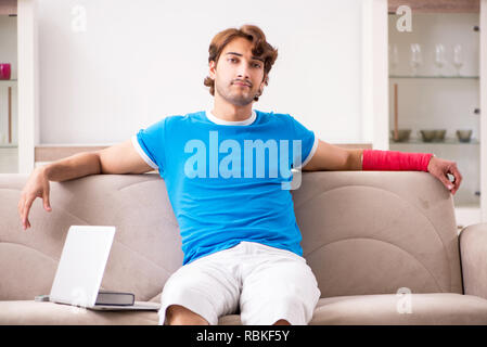 Young man with injured arm sitting on the sofa Stock Photo