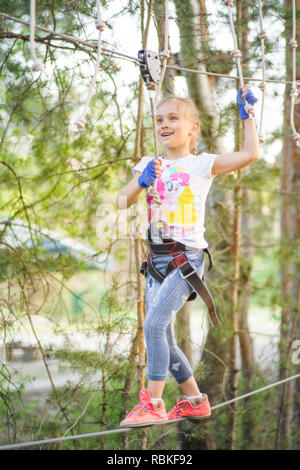 Girl in the rope park pass obstacles, girl climb the road .Rope park on a summer sunny day. Stock Photo