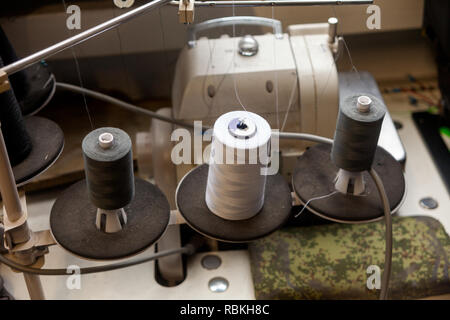 Three big black and white bobbins with large mating threads mounted on a rod near the sewing machine on the table of the workshop in the studio fot ca Stock Photo