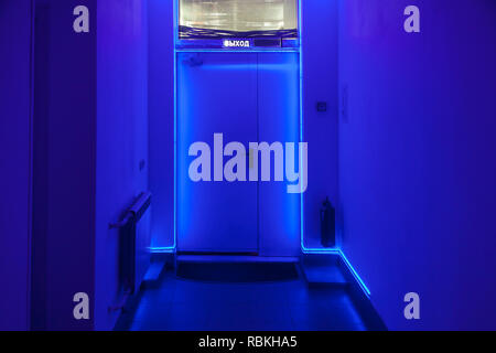 Dark corridor with a door at the end of the tunnel with blue LED illumination around the perimeter and an inscription exit at the top Stock Photo