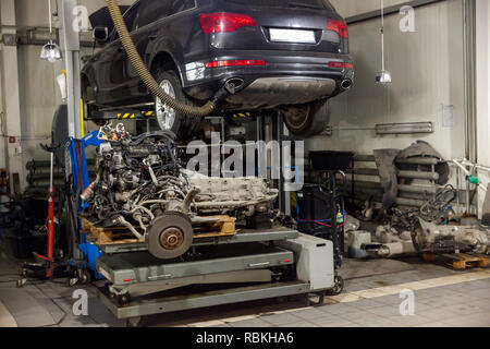A sports car raised on a lift for repair and under it a detached engine ...