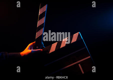 Opened clapperboard for cinema in hand, before filming on a black isolated background with red and blue backlighting Stock Photo