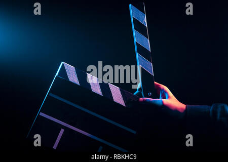 Opened clapperboard for cinema in hand, before filming on a black isolated background with red and blue backlighting Stock Photo