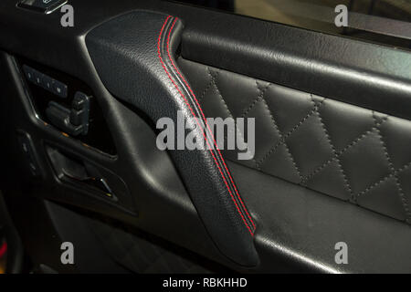 A view of a part of the interior of the car door from leather of black color, stitched double thread of red color with contrast stitching in a vehicle Stock Photo