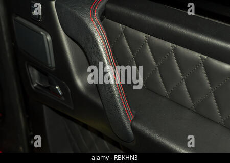A view of a part of the interior of the car door from leather of black color, stitched double thread of red color with contrast stitching in a vehicle Stock Photo
