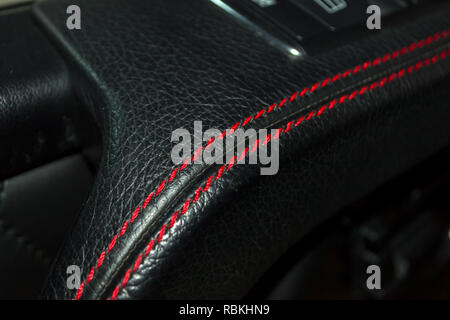 A view of a part of the interior of the car door handle from leather of black color, stitched double thread of red color with contrast stitching in a  Stock Photo