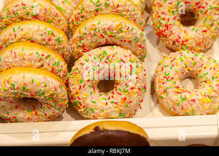 Appetizing big white donuts with white icing and multi-colored confetti, made according to homemade recipe, laid out in the window of the grocery stor Stock Photo