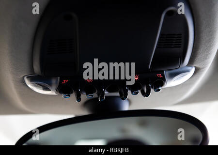 Lighting control inside the car from the top on the instrument panel behind the rear-view mirror in black with buttons and red illumination close-up. Stock Photo