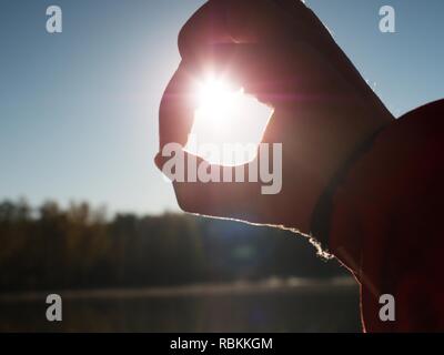 Hands catch sun at sunset time. Female fingers hold sun above lake level. Stock Photo
