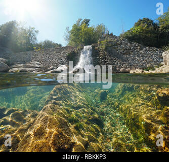 Old stone dam on the river with rocks underwater, split view half above and below water surface, Sant Llorenc de la Muga, Catalonia, Spain Stock Photo