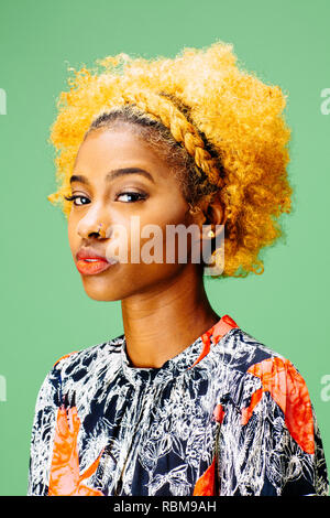 Portrait of a lovely young girl with bleached curly hair looking at camera, in front of a green bac Stock Photo