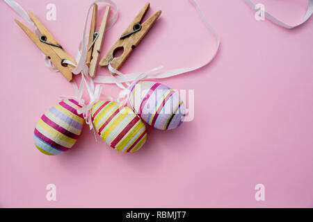 colorful Easter Eggs with Cross hanging on line from clothespins.Still Life Easter eggs hanging on a rope on pink background. Easter holiday concept.Copy space Stock Photo