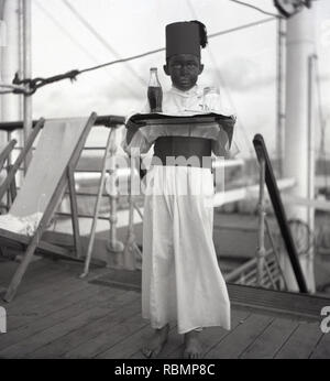 1950s, historical, Union-Castle Steamship, young boy in a fancy dress competition on the deck of a ship dressed in a costume as a foreign (egyptian) waiter and holding a tray with a soft drink bottle. Stock Photo