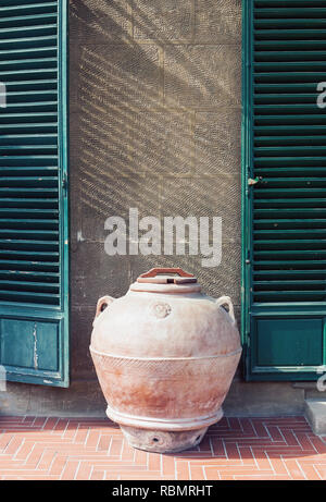 Antique clay jar standing by the wall of an old house in Italy, vertical oriented outdoor picture Stock Photo
