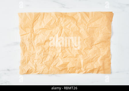 Crumpled piece of parchment or baking paper on white marble table. Top view. Copy space for text and design element. Stock Photo