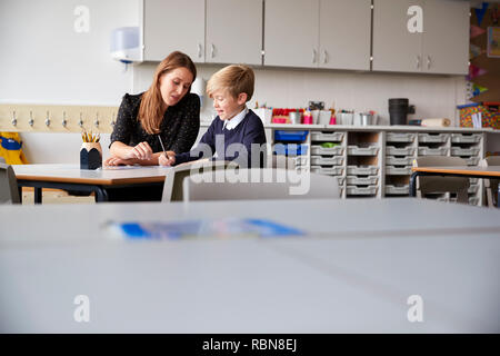 Young female primary school teacher and schoolboy sitting at a table working one on one, selective focus Stock Photo