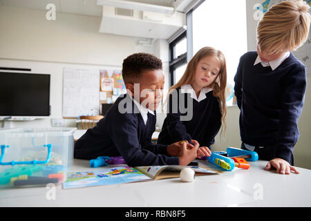 Three primary school children standing at a table in a classroom working together with toy construction blocks, close up, low angle Stock Photo