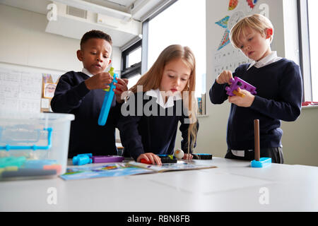 Three primary school children working together with toy construction blocks in a classroom, the girl reading instructions from a book, close up, low angle Stock Photo