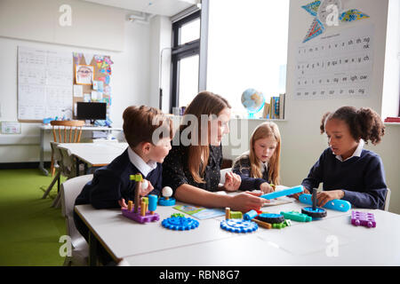 Female teacher and three primary school kids sitting at a table in a classroom working with educational construction toys Stock Photo