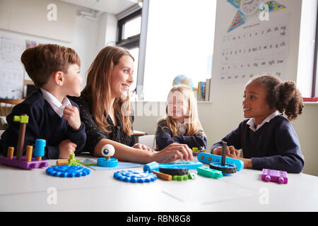 Female teacher and three primary school kids sitting at a table in a classroom working with educational construction toys, close up, low angle Stock Photo