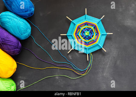 Handmade mandala of multicolor blue, purple, yellow yarn threads on dark grey background. Stock Photo