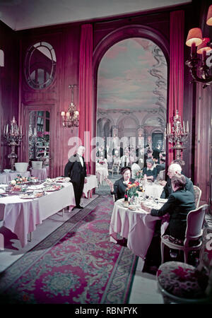 Mid twentieth century colour photograph taken inside the Ritz Hotel in London, showing the opulence of the dining experience. Photo shows  the waiting staff, plus many people enjoying tea or dinner in the hotel. Taken around 1950. Stock Photo