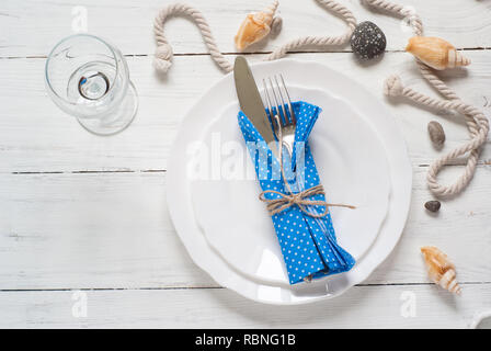 Marine table setting with white dishes and sea decorations at white wooden table. Top view. Stock Photo