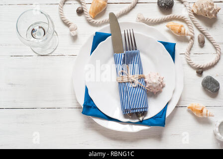 Marine table setting with white dishes and sea decorations at white wooden table. Top view. Stock Photo