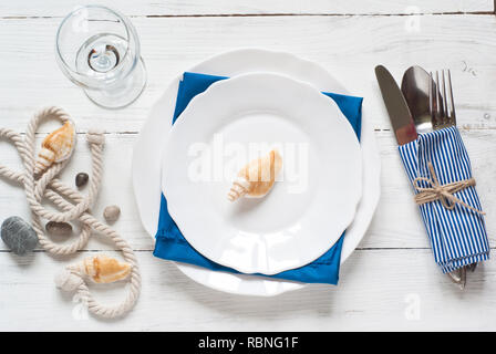 Marine table setting with white dishes and sea decorations at white wooden table. Top view. Stock Photo