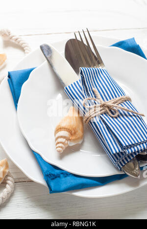 Marine table setting with white dishes and sea decorations at white wooden table. Top view. Stock Photo