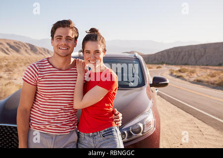 Young white couple standing on desert roadside by car Stock Photo