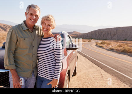 Senior white couple standing on desert roadside by car Stock Photo