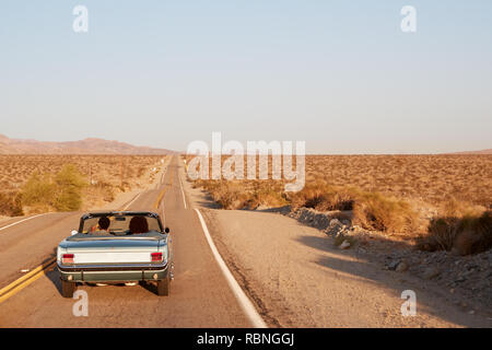Couple driving convertible car on desert highway, back view Stock Photo