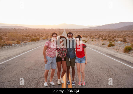 Four friends standing on a desert highway smiling to camera Stock Photo