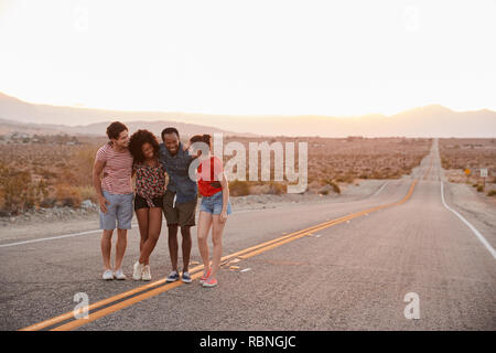 Four young adult friends standing on desert highway talking Stock Photo