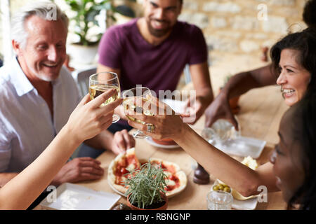 Smiling friends eating at a table in a cafe making a toast Stock Photo