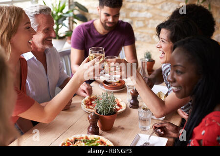 Friends laughing at a dining table in a cafe making a toast Stock Photo