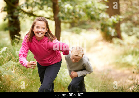 Two children walking in a forest amongst greenery smiling at camera, front view, focus on foreground Stock Photo