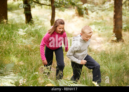 Two children walking together in a forest amongst greenery, three quarter length, side view Stock Photo