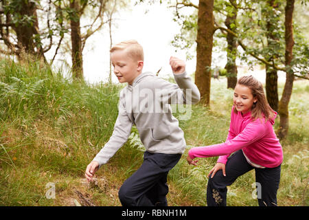 Two children walking together through a forest by tall grass, side view Stock Photo