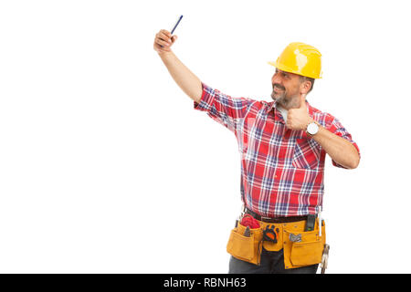 Happy friendly male builder taking selfie holding thumb up as like gesture isolated on white background Stock Photo